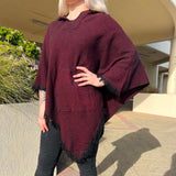 Person wearing a burgundy poncho outdoors on a sunny day.