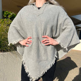 Person wearing a gray poncho with fringes standing outdoors.