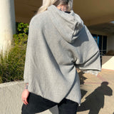 Person wearing a gray hooded poncho standing outdoors on a sunny day.