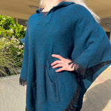 Person wearing a blue poncho with fringe details outdoors.