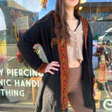 Woman wearing a black cardigan with colorful patterns in front of a store window.