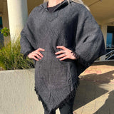 Person wearing a dark gray poncho standing outdoors on a sunny day.