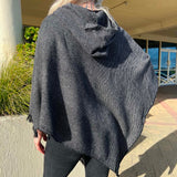 Person wearing a dark gray poncho outdoors on a sunny day.