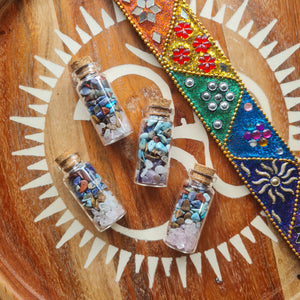 Small glass bottles with colorful crystal chips on a wooden surface with decorative elements.